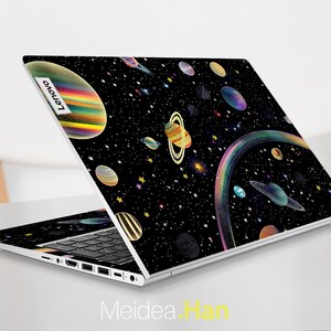 May include: A black laptop with a space-themed design featuring planets, stars, and a rainbow. The laptop is open and the Lenovo logo is visible on the back.