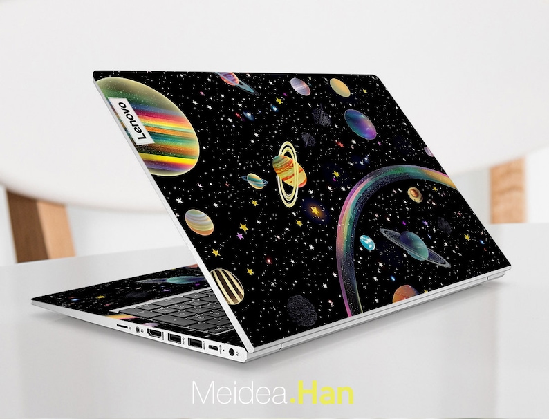 May include: A black laptop with a space-themed design featuring planets, stars, and a rainbow. The laptop is open and the Lenovo logo is visible on the back.