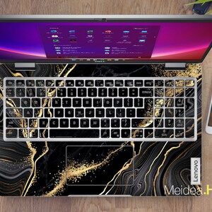 Puede incluir: Un port&aacute;til negro con un dise&ntilde;o de m&aacute;rmol dorado y negro en el teclado y el touchpad. La pantalla del port&aacute;til est&aacute; encendida y muestra un escritorio con varias ventanas abiertas. El port&aacute;til tiene el logotipo de Lenovo en la esquina inferior derecha. El texto "Meidea.Han" est&aacute; en la esquina inferior izquierda.