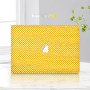 Könnte beinhalten: Eine gelbe Laptop-Haut mit einem Karbonfaser-Muster. Die Haut hat ein weißes Apple-Logo in der Mitte.