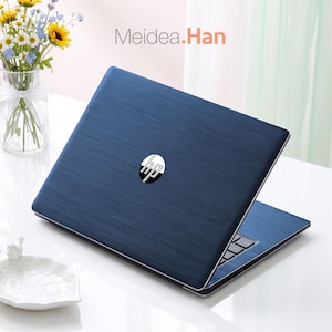 May include: A dark blue HP laptop with a brushed metal texture on the lid and a centred silver HP logo. The text Meidea.Han is visible above the laptop. The device is positioned on a white surface next to a clear glass vase containing flowers.