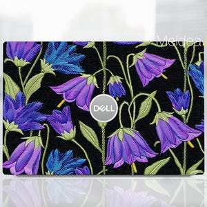 May include: A laptop skin featuring a floral design with purple and blue bellflowers on a black background. The skin has a Dell logo in the center. The flowers have green stems and leaves.