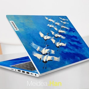 May include: A Lenovo laptop with a vibrant blue cover featuring a painting of white cranes in flight against a blue sky. The laptop is open, displaying the keyboard and screen. The Lenovo logo is visible.