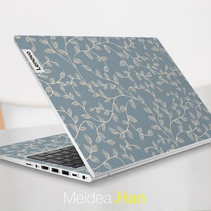 May include: A Lenovo laptop with a light blue cover featuring a repeating pattern of beige vines and leaves. The laptop is open, displaying the keyboard and ports. The Lenovo logo is visible on the top left corner.