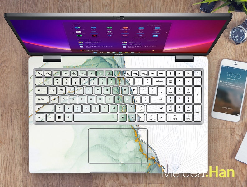 Może przedstawiać: Biały laptop z zielonym i złotym marmurowym wzorem na pokrywie i klawiaturze. Laptop jest otwarty, a ekran wyświetla pulpit z fioletowym tłem.