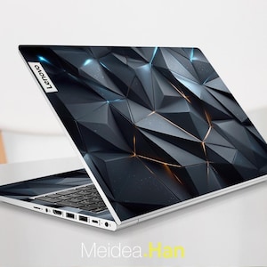 May include: A silver Lenovo laptop with a geometric design on the lid. The design features a dark gray, three-dimensional pattern with orange and blue highlights. The Lenovo logo is visible in the upper left corner.