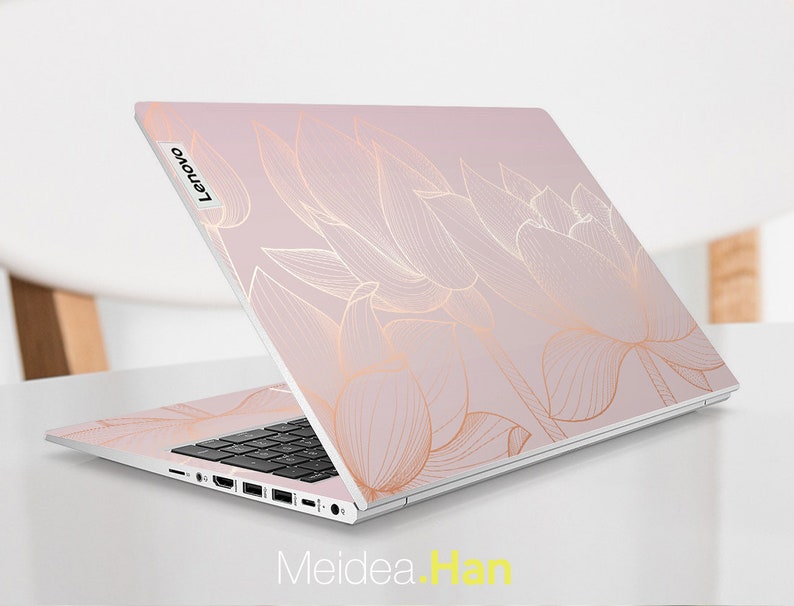 Puede incluir: Un port&aacute;til Lenovo con un dise&ntilde;o floral rosa claro. El dise&ntilde;o presenta dibujos lineales dorados de flores de loto. El port&aacute;til est&aacute; abierto, revelando un teclado negro y el logotipo de Lenovo. El texto "Meidea.Han" es visible.