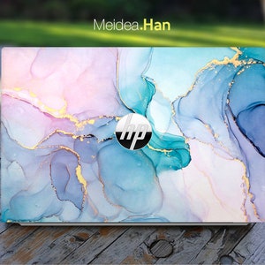 Puede incluir: Una piel para portátil con un diseño abstracto que presenta remolinos de azul, rosa y morado con acentos dorados. El logotipo de HP es visible en el portátil.