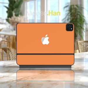 Pode incluir: Capa de tablet laranja com o logotipo branco da Apple. A capa está aberta, revelando a tela. O texto "Meidea.Han" é visível no fundo. A capa está sobre uma superfície de mármore.