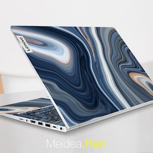 May include: A Lenovo laptop with a blue, white, and tan marble design. The laptop is open, displaying the keyboard and ports. The design covers the lid and the area around the keyboard. The Lenovo logo is visible on the top left corner of the lid.
