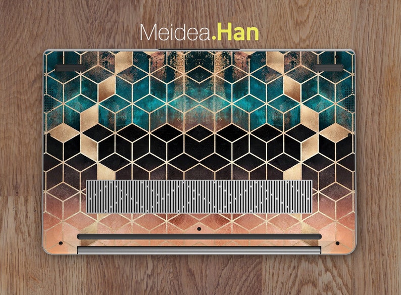 May include: A laptop with a geometric pattern on the back. The pattern is made up of gold and teal cubes on a black background. The laptop is on a wooden surface.