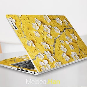 May include: A yellow laptop with a white floral design on the lid. The laptop has a black keyboard and a silver bottom. The Lenovo logo is visible on the lid.