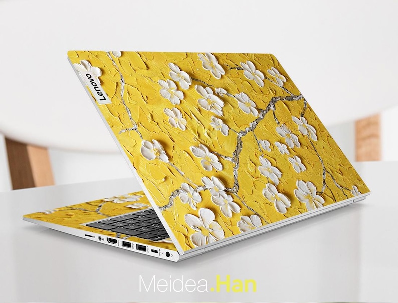 May include: A yellow laptop with a white floral design on the lid. The laptop has a black keyboard and a silver bottom. The Lenovo logo is visible on the lid.