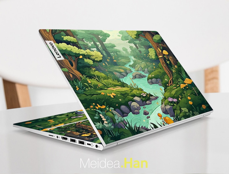 May include: A white laptop with a colorful cartoon forest scene on the lid. The scene features a winding river, green trees, and yellow mushrooms. The laptop has the Lenovo logo on the lid.