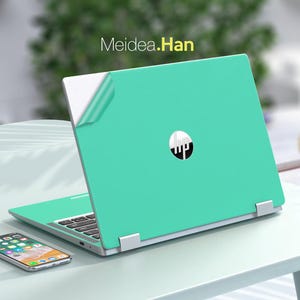 Könnte beinhalten: Ein türkisfarbener Laptop mit einem silbernen HP-Logo auf dem Deckel. Der Laptop ist geöffnet und der Bildschirm ist aus. Der Laptop steht auf einem weißen Tisch mit einem weißen Telefon daneben.