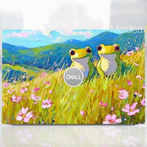 May include: A laptop skin with an impressionistic painting of two cartoon frogs in a field of wildflowers. The background shows rolling hills and a blue sky. The Dell logo is visible in the centre.