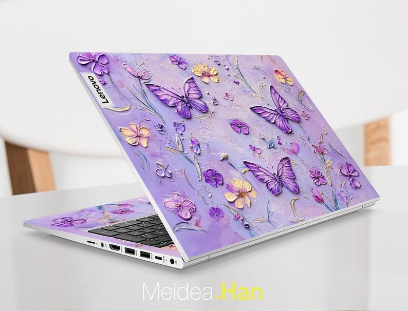 May include: A purple laptop with a floral design featuring butterflies and flowers. The laptop has a silver Lenovo logo on the lid.