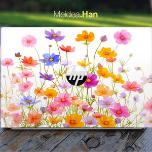 Puede incluir: Un portátil blanco con un diseño floral con flores rosas, amarillas, naranjas, azules y moradas. El portátil tiene un logotipo de HP en la tapa.