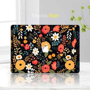 May include: A black laptop skin with a floral pattern featuring red, yellow, and white flowers on a black background. The design includes leaves and stems.