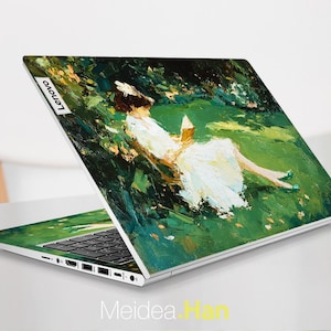 Puede incluir: Un port&aacute;til Lenovo con una cubierta personalizada que presenta una pintura impresionista de una persona reclinada en un campo verde, leyendo un libro. La obra de arte utiliza una paleta de verdes, blancos y amarillos. El port&aacute;til est&aacute; abierto, mostrando el teclado y la pantalla.