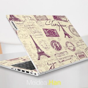 May include: A white laptop with a cream-colored design featuring a repeating pattern of Eiffel Towers and vintage stamps. The laptop has a black keyboard and a silver Lenovo logo.