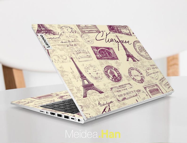May include: A white laptop with a cream-colored design featuring a repeating pattern of Eiffel Towers and vintage stamps. The laptop has a black keyboard and a silver Lenovo logo.