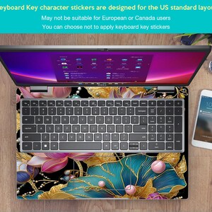 May include: Laptop with a floral design keyboard skin. The skin features gold, teal, pink, and black colors. The keyboard has standard US layout keys. The screen displays a colorful interface. A smartphone and watch are also visible.