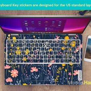 May include: A laptop computer with a floral keyboard sticker. The sticker features a dark blue background with pink, yellow, and white flowers and stems. The laptop is a Lenovo.