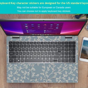 May include: Laptop with a keyboard skin featuring a light blue background and a white leaf pattern. The laptop screen displays a colorful interface. A smartphone and a watch are visible on the wooden surface. Text on the image states: "Keyboard Key character stickers are designed for the US standard layout."