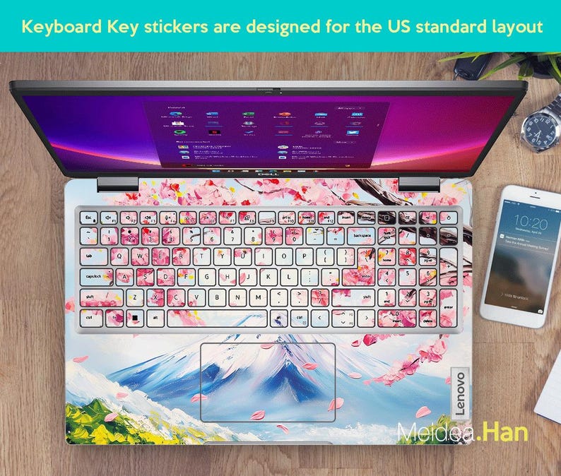 May include: A laptop computer with a pink and white cherry blossom design keyboard sticker. The sticker features a mountain scene with a blue sky and white clouds. The text "Lenovo" and "Meidea.Han" are visible on the laptop.