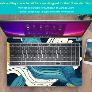 May include: A laptop computer with a blue and white abstract design keyboard sticker. The sticker features a swirling pattern of blue and white lines on a dark background. The laptop is open and the screen is displaying a desktop with multiple icons.
