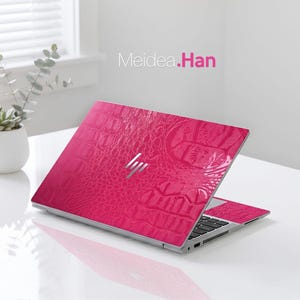 May include: A hot pink laptop with a textured, crocodile-skin pattern. The laptop is open, displaying the keyboard and screen. The HP logo is visible. The text "Meidea.Han" is in the upper right corner.