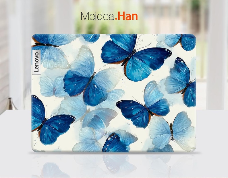 May include: A laptop case featuring a pattern of blue butterflies on a cream background. The butterflies vary in size and shade, with some appearing more translucent. The Lenovo logo is visible on the left side, and the text "Meidea.Han" is at the top.
