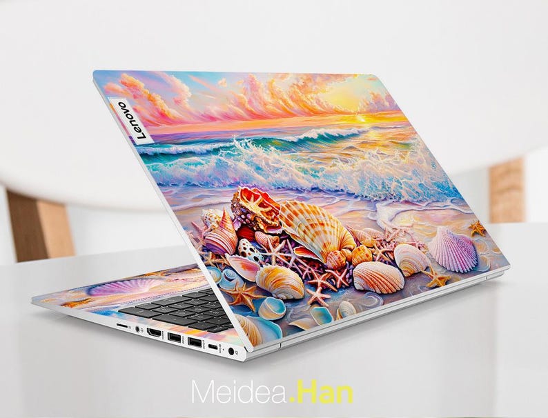 Op de afbeelding: Een laptop met een kleurrijk schelpdesign op de deksel. Het ontwerp toont een zonsondergang boven de oceaan met golven die op de kust breken. De laptop is open en het toetsenbord is zichtbaar. Het Lenovo-logo is zichtbaar op de deksel.