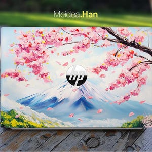 May include: A laptop with a painted design featuring a mountain scene with cherry blossoms. The design includes a mountain, pink flowers, and a blue sky. The HP logo is visible. The text "Meidea.Han" is in the upper left corner.