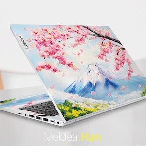 May include: A white laptop with a colorful design on the lid. The design features a mountain range with pink cherry blossoms and blue sky. The laptop has a black keyboard and a silver Lenovo logo on the lid.
