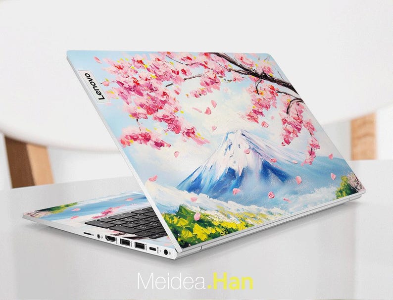 May include: A white laptop with a colorful design on the lid. The design features a mountain range with pink cherry blossoms and blue sky. The laptop has a black keyboard and a silver Lenovo logo on the lid.
