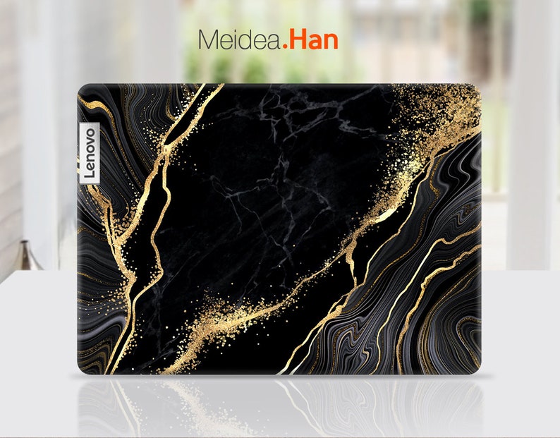 Puede incluir: Piel negra para port&aacute;til con un dise&ntilde;o de m&aacute;rmol dorado. La piel tiene un efecto de brillo sutil y la palabra "Lenovo" est&aacute; impresa en el lado izquierdo.