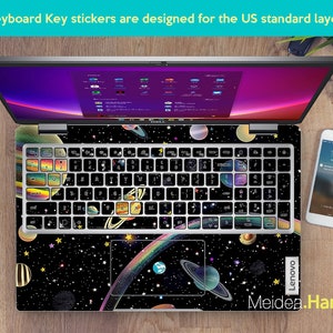 May include: A laptop computer with a black and white space-themed keyboard sticker set. The sticker set features planets, stars, and a rainbow. The laptop is a Lenovo.