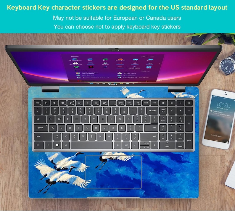 May include: Laptop with a keyboard skin featuring a blue and white crane design. The keyboard has standard US layout keys. The screen displays a colorful interface. A smartphone and watch are visible on the wooden surface.