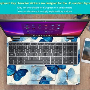 May include: Laptop with a keyboard skin featuring a blue butterfly design. The keyboard has a standard US layout. The screen displays a colorful interface. A smartphone and watch are visible on the wooden surface.
