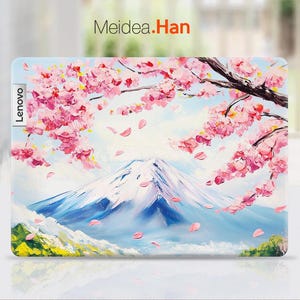 May include: A laptop skin featuring a colorful painting of a mountain range with pink cherry blossoms in the foreground. The text "Lenovo" is printed on the left side of the skin and "Meidea.Han" is printed at the top.