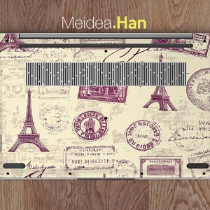 May include: A laptop skin with a vintage Parisian theme. The design features a cream background with purple stamps and illustrations of the Eiffel Tower, Parisian street signs, and other Parisian landmarks.