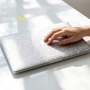 Könnte beinhalten: Ein silberner Laptop mit einer geometrischen Musterabdeckung. Der Laptop hat ein weißes Apple-Logo auf der Oberseite. Der Text "Meidea Han" ist in der oberen linken Ecke sichtbar. Eine Hand liegt auf dem Laptop.