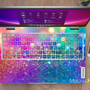 May include: A laptop computer with a colorful glitter keyboard cover and a matching glitter design on the bottom. The screen is displaying a desktop with multiple icons. The laptop is on a wooden surface.