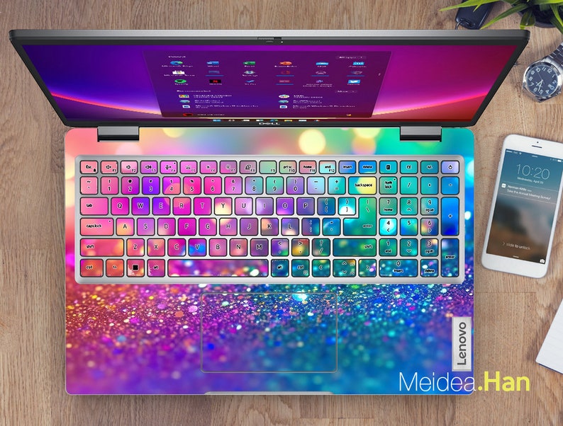 May include: A laptop computer with a colorful glitter keyboard cover and a matching glitter design on the bottom. The screen is displaying a desktop with multiple icons. The laptop is on a wooden surface.