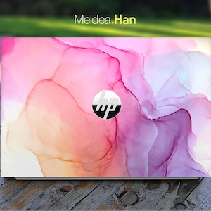 May include: A white laptop with a pink, purple, and orange abstract design on the lid. The HP logo is visible in the center of the lid.