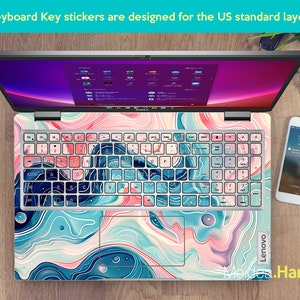 Op de afbeelding: Een laptoptoetsenbord met kleurrijke abstracte stickers. De stickers hebben een draaiend patroon in blauw, roze en wit. Het toetsenbord is gelabeld met "Lenovo".