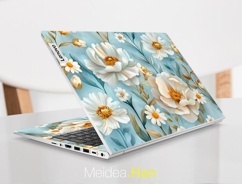 Puede incluir: Un port&aacute;til blanco con un dise&ntilde;o floral azul y blanco en la tapa. El dise&ntilde;o presenta grandes flores blancas con centros amarillos y flores blancas m&aacute;s peque&ntilde;as con centros amarillos. El port&aacute;til est&aacute; abierto y el teclado es visible.