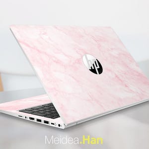 May include: A pink marble-patterned laptop skin on an HP laptop. The laptop is open, revealing a black keyboard and the HP logo. The skin covers the lid and the palm rest area. The text "Meidea.Han" is at the bottom.